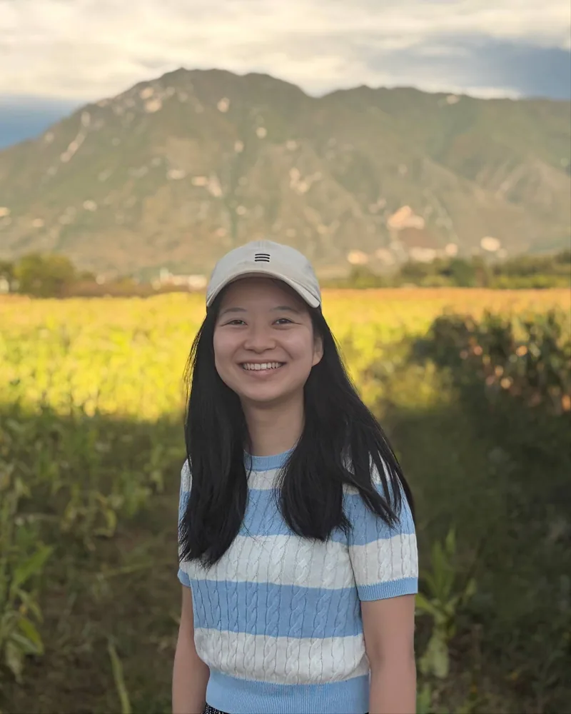 Portrait of Mingwei outdoors in front of a mountain landscape